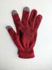 Single red touchscreen glove with gray fingertips isolated on a white background. Top view flat lay of a knitted winter accessory.