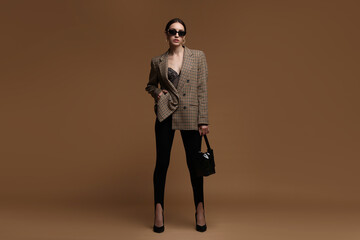 Full-length portrait of beautiful woman in stylish outfit on brown background