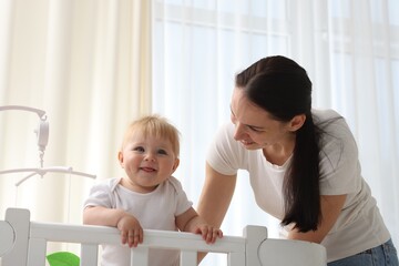Mother playing with her cute baby in crib at home