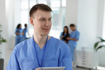 Medical student in uniform with tablet indoors, selective focus