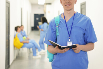Medical student in uniform with backpack and notebook at university, selective focus
