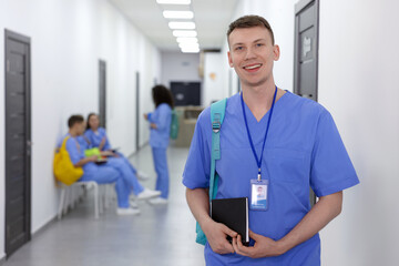 Medical student in uniform with backpack and notebook at university, selective focus
