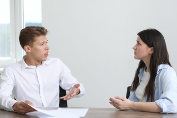 Young woman complaining to man at wooden table indoors