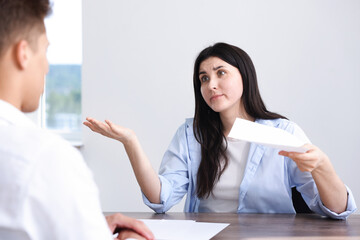 Young woman complaining to man at wooden table indoors