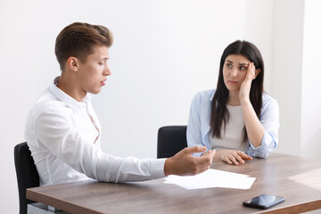 Young man complaining to woman at wooden table indoors