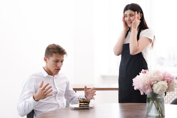 Young man complaining to waiter about cake at table in restaurant