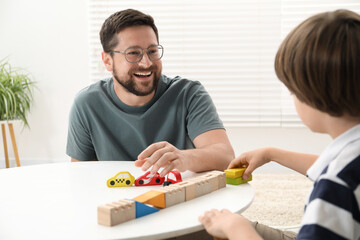 Father and son playing with wooden figures at white table indoors