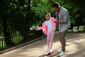 Obraz premium Family getaway. Happy father and daughter having fun with penny board in park. Space for text