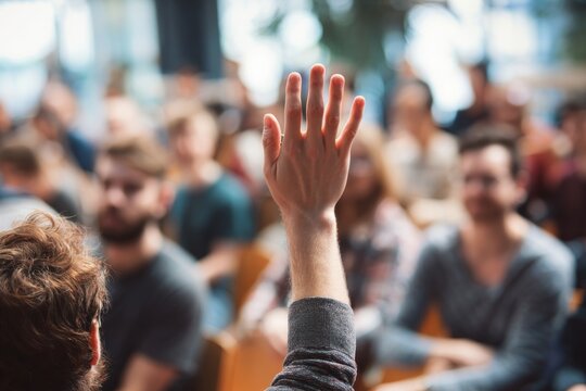 Engaged audience member raises hand during a question-and-answer session at a seminar, showing active participation and interest in the presentation.