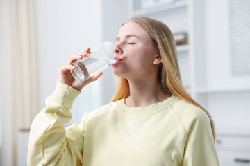 Young woman drinking water from glass at home