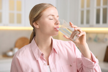 Young woman drinking water from glass in kitchen