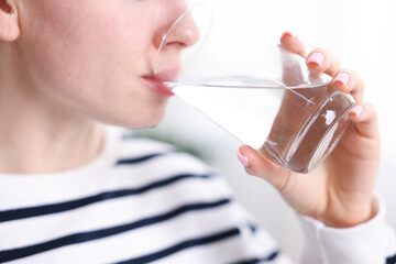 Young woman drinking water from glass at home, closeup