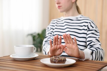 Gluten free diet. Woman refusing from donut at wooden table indoors, closeup