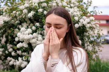 Woman suffering from seasonal pollen allergy near blossoming shrub on spring day
