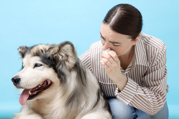 Woman suffering from allergy with her dog on light blue background