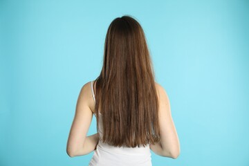 Obraz premium Woman with long hair on light blue background, back view