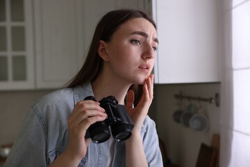 Paranoia. Worried woman with binoculars in kitchen
