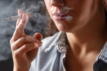 Fototapeta premium Woman in shirt smoking cigarette on dark background, closeup. Bad habit