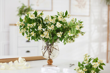 Bouquet of beautiful jasmine flowers in vase on white table indoors