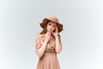 A woman in a beautiful brown dress and a fashionable hat stands on a white background.