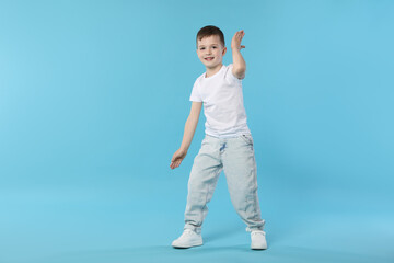 Happy little boy dancing on light blue background. Space for text