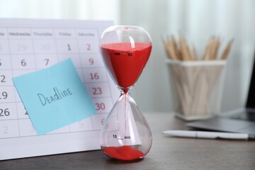 Sticky note with word Deadline, calendar and hourglass with flowing sand on table indoors, closeup
