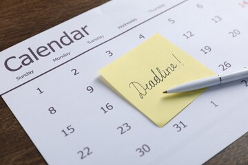 Sticky note with word Deadline, calendar and pen on wooden table, closeup