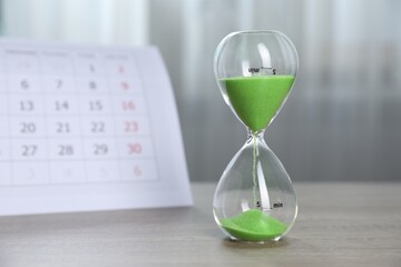 Deadline. Hourglass with flowing sand and calendar on wooden table indoors