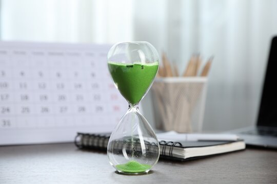 Deadline. Hourglass with flowing sand, stationery, calendar and laptop on wooden table indoors