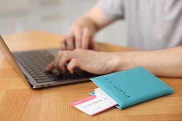 Man using laptop at wooden table with passport and flight ticket indoors, closeup