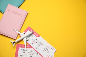 Passports with tickets and airplane model on yellow background, flat lay. Space for text