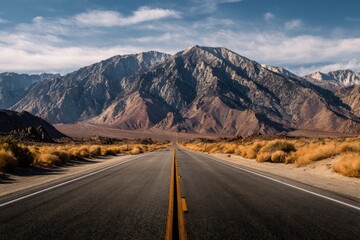 Fototapeta premium Mountain road with asphalt leading to majestic mountain range under blue sky, perfect for scenic travel and adventure.