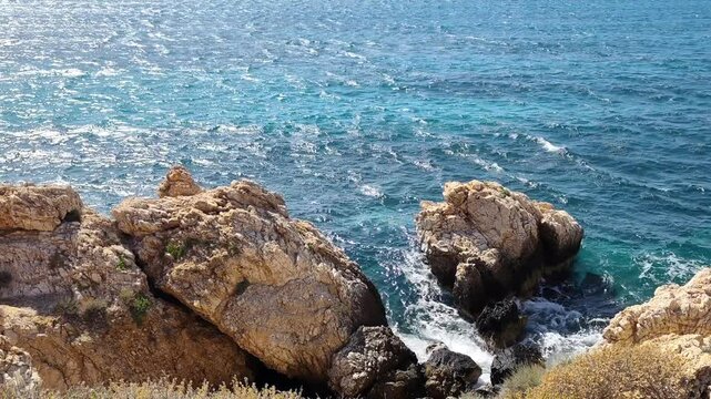 Video of the turquoise waves of the Aegean Sea splashing against the rocky shore of Paros Island in the Cyclades, Greece, creating a stunning display of natural beauty and power.