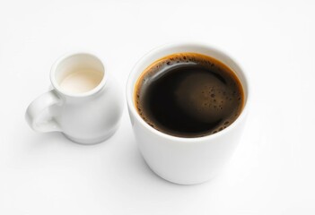 Fototapeta premium Frothy black coffee in a pristine white cup beside a milk creamer on a white background, ceramic cup, black coffee