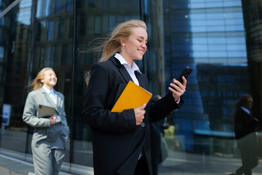 Young professionals walk confidently in a modern city while engaging with their mobile devices and enjoying teamwork