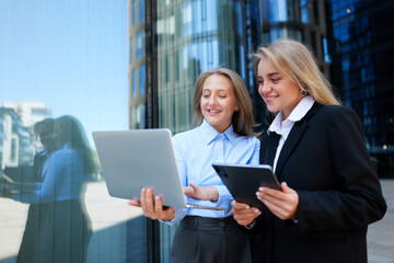 Business professionals collaborate with digital devices outside modern glass office building during...