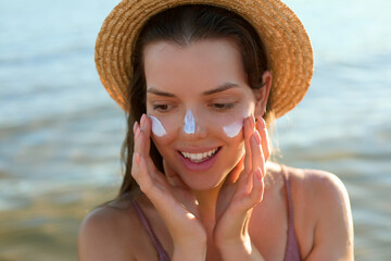 Beautiful young woman at beach applying sunscreen on face. Beauty girl applying suntan lotion at...