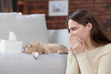 Woman suffering from allergy with her cat at home, selective focus