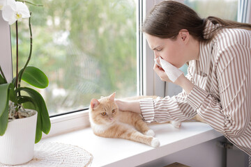 Woman suffering from allergy with her cat near window at home