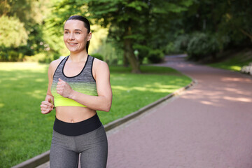 Sporty woman running in park, space for text