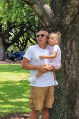 Father holds his little daughter in his arms in a city park. They look away in surprise, because...