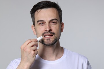 Man applying lip balm onto his lips on grey background