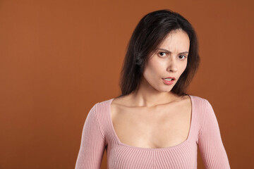 Portrait of confused woman on brown background, space for text
