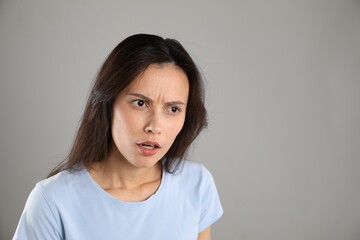 Portrait of shocked woman on grey background, space for text