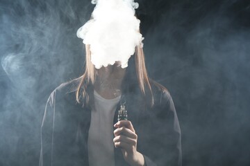 Woman using electronic smoking device on dark background