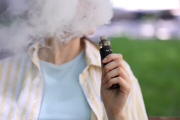 Young woman using electronic smoking device outdoors, closeup