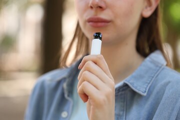 Young woman using electronic smoking device outdoors, closeup