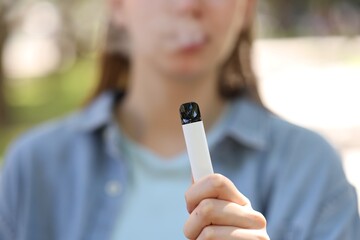 Young woman using electronic smoking device outdoors, closeup