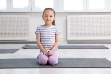 Cute girl sitting on yoga mat indoors