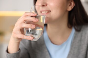 Woman drinking water from glass in kitchen, closeup